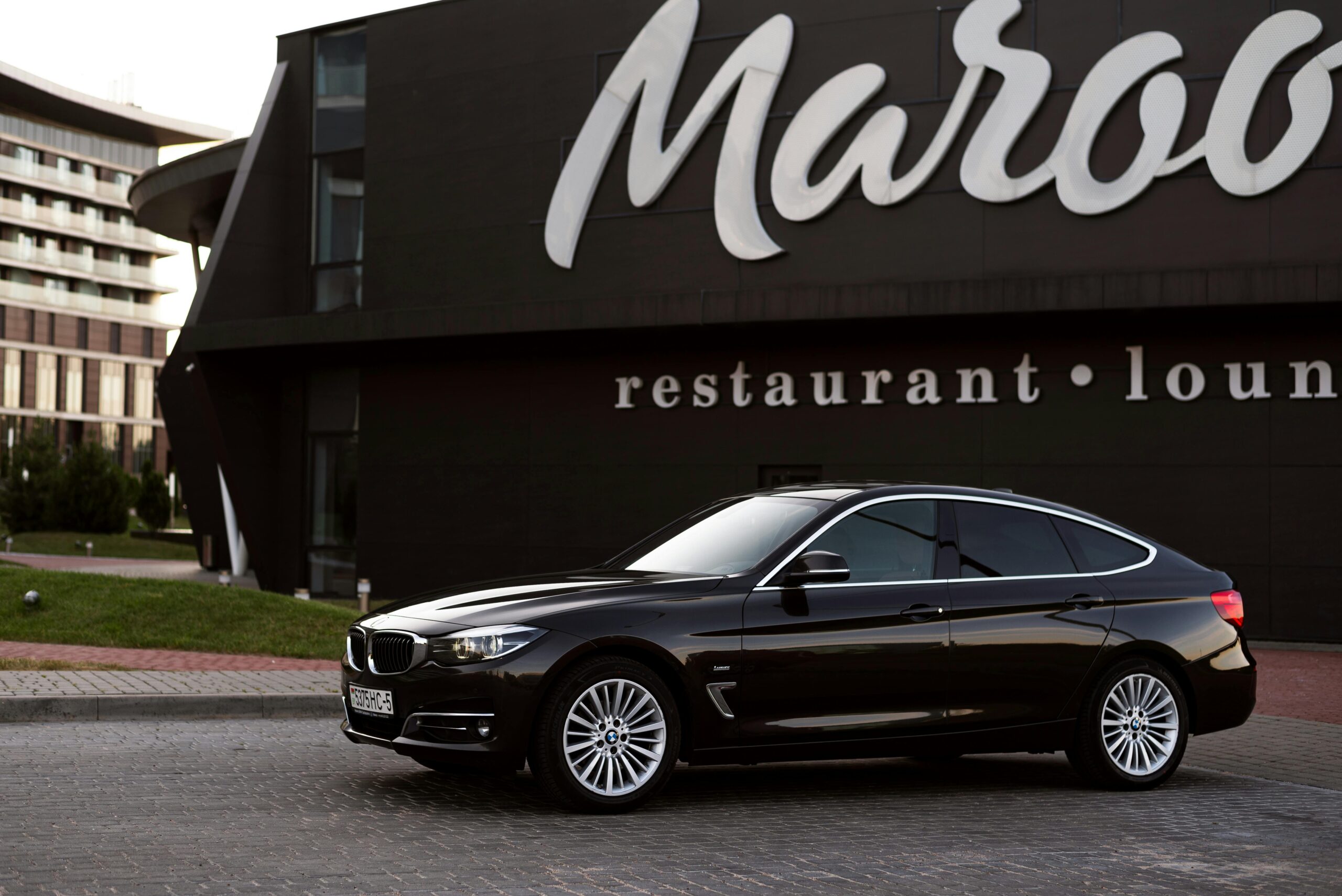 Black BMW sedan parked in front of stylish modern building with lounge signage, showcasing luxury and elegance.